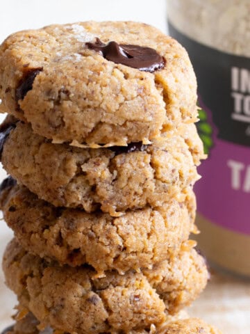 A stack of keto tahini cookies with chocolate chips and topped with sea salt flakes, with a jar of tahini in the background.