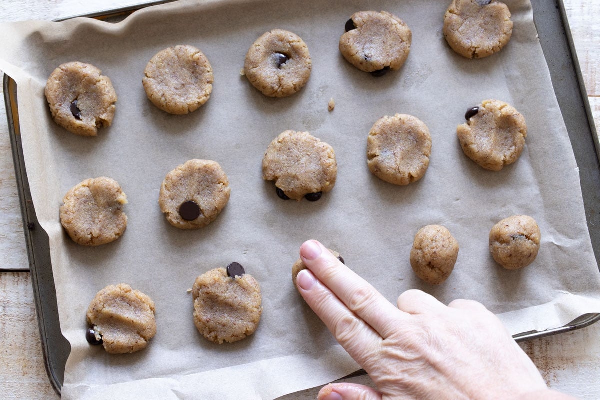 Pressing down the tahini cookie dough balls into round cookie shapes with 2 fingers.