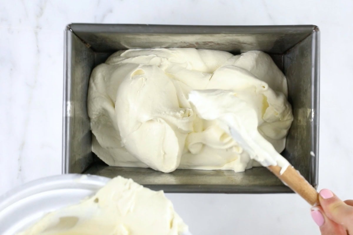 Spooning the ice cream into a metal container with a spatula.
