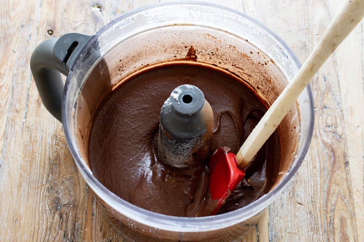 Chocolate cake batter in a food processor bowl and a spatula.