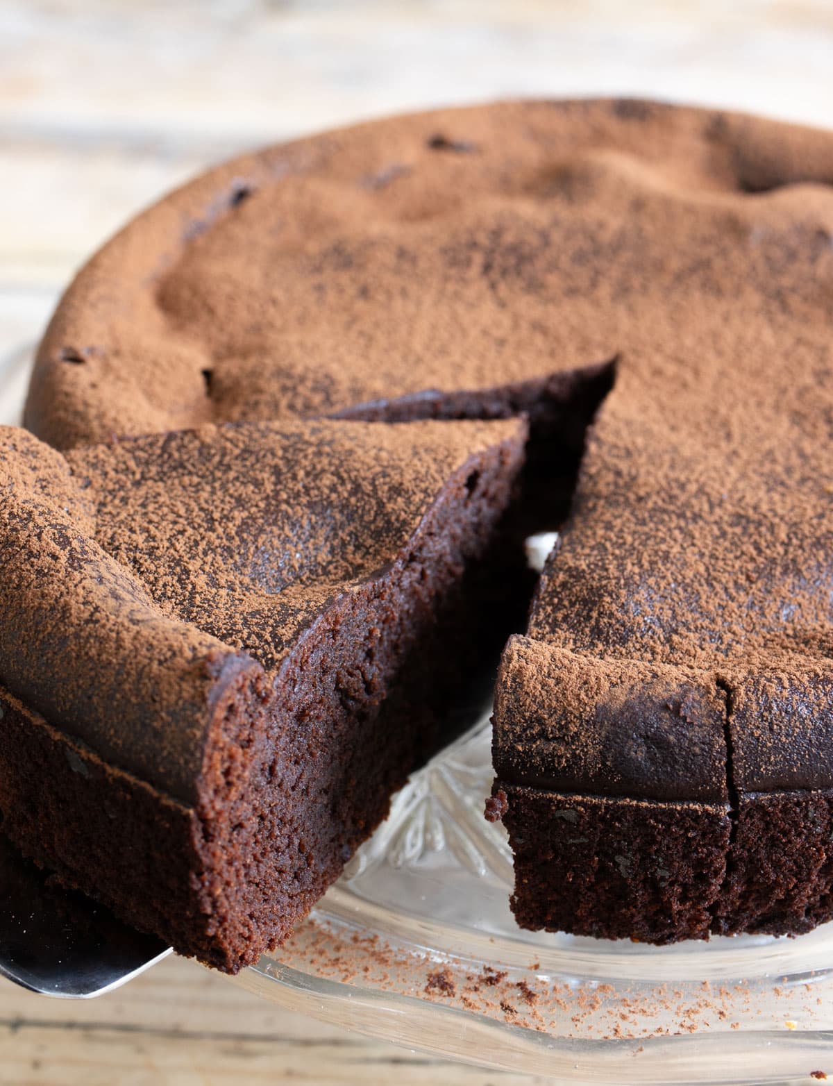 Taking a slice of cottage cheese chocolate cake from a cake on a glass cake stand.