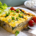 A slice of cottage cheese egg bake with sounach and musnrooms topped with spring onion on a plate with cherry tomatoes and chopped letuce.