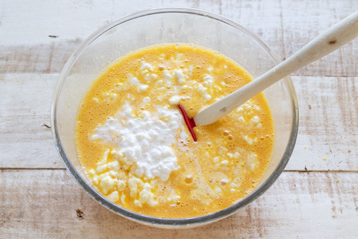 Cottage cheese in the beaten egg mixture in a bowl with a spatula.