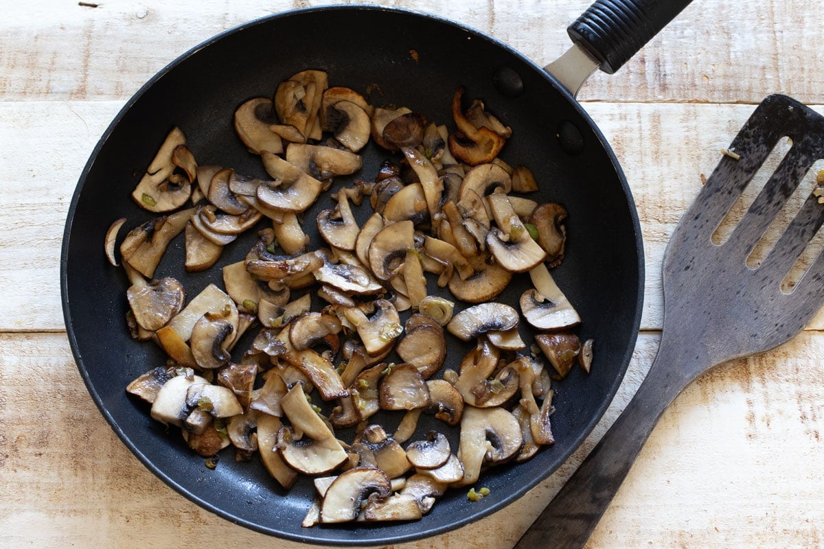 Sauteed mushrooms sliced in a skillet and a spatula.