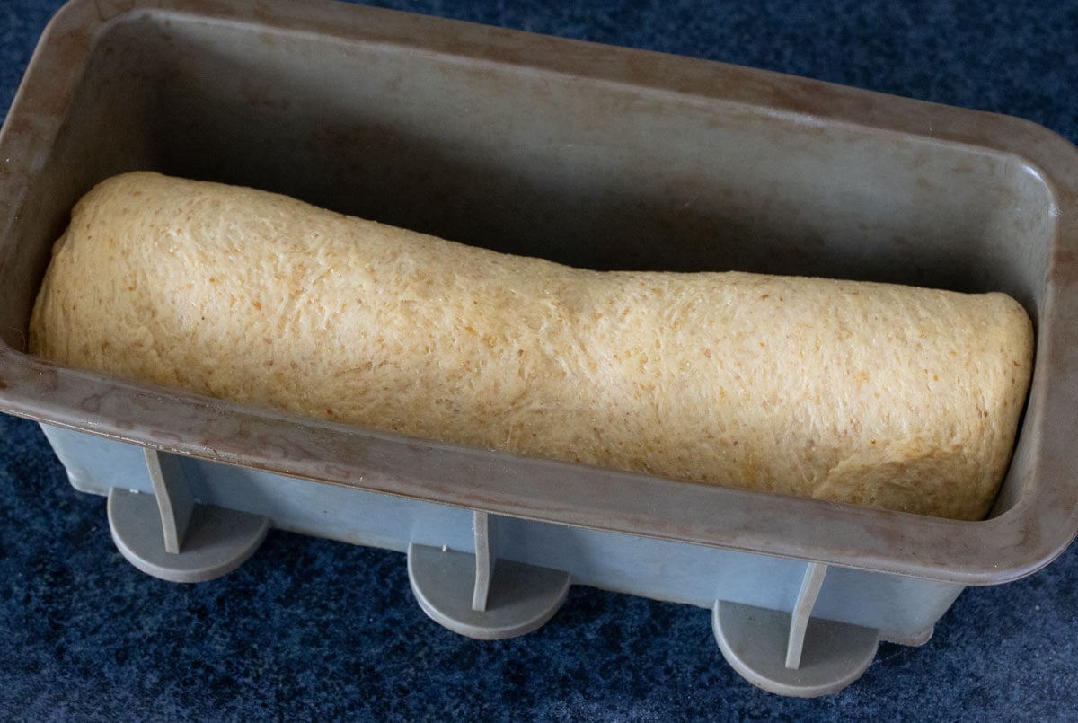 Placing the dough seam side down into a rectangular silicone bread pan.