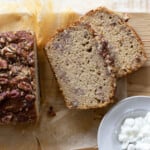 Cottage cheese banana bread loaf with 2 slices topped with crushed pecans and a small bowl of cottage cheese.