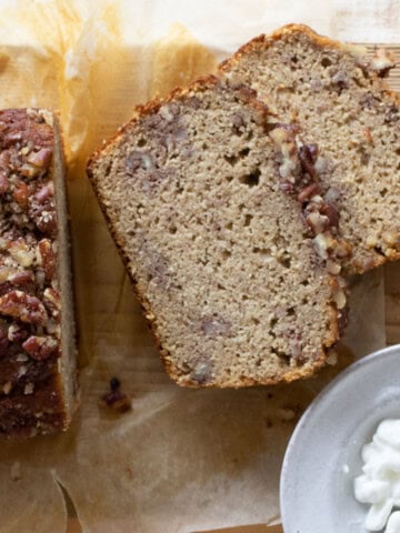 Cottage cheese banana bread loaf with 2 slices topped with crushed pecans and a small bowl of cottage cheese.