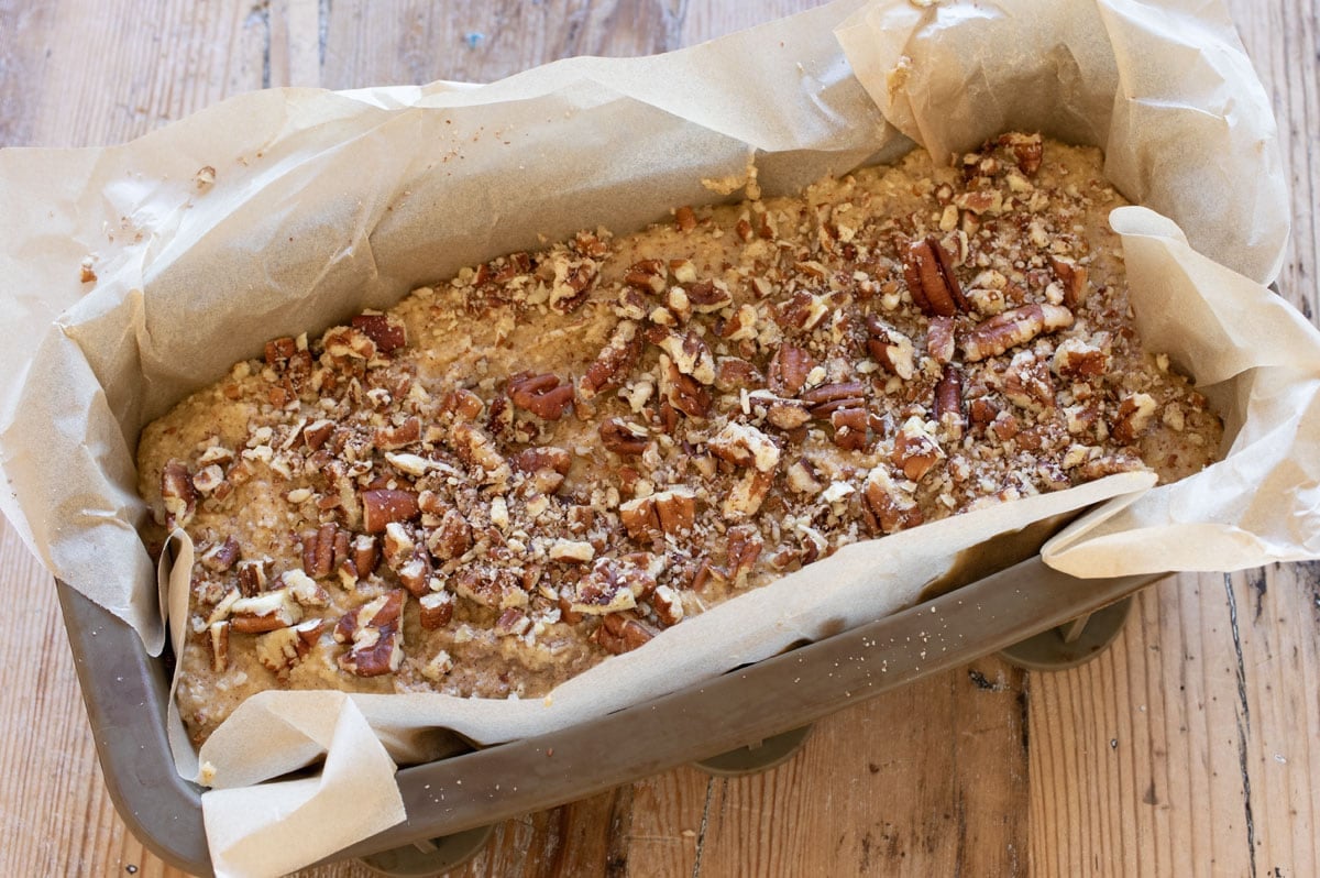 The batter in a parchment paper lined silicone loaf pan, topped with crushed pecans.