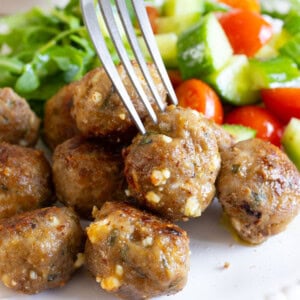 Fork taking a lamb meatball from a plate.