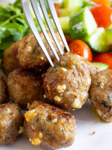 Fork taking a lamb meatball from a plate.