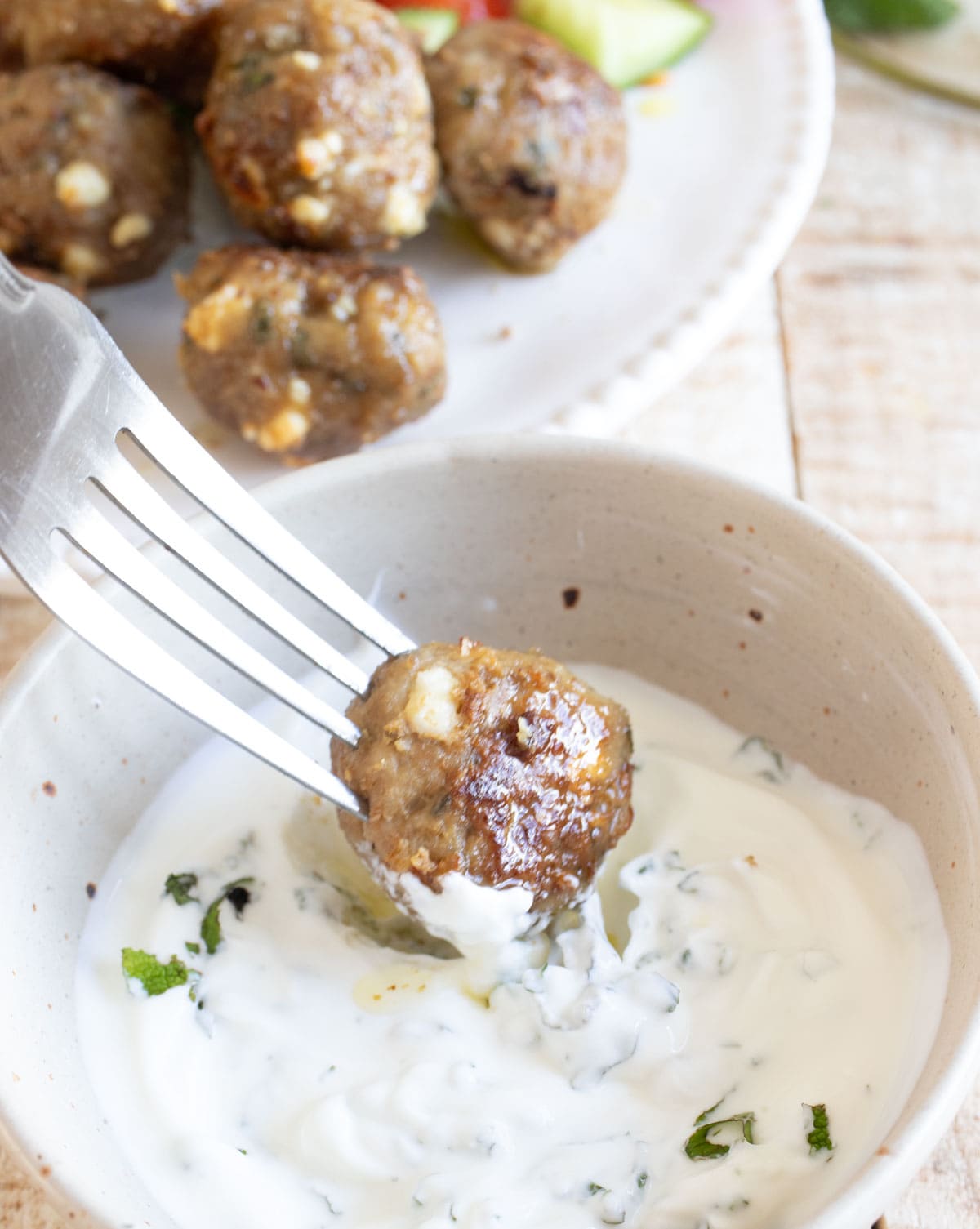 Fork dipping a lamb meatball into a bowl with tzatziki.